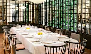 Et opdækket bord i en restaurant med elegante stole og store vinduer med grønt udenfor. (AI-genereret tekst)