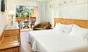 Et hotelværelse med to enkeltsenge, en lænestol og en møbleret altan i baggrunden. (AI-genereret tekst)