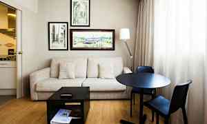 Et værelse med sofa, bord og to stole, vægdekorationer og et lille køkken. (AI-genereret tekst)