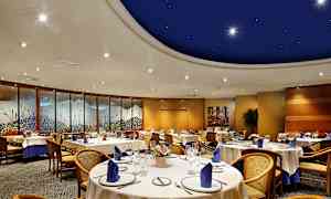 En elegant indrettet spisesal med runde borde og stole, dekoreret med blå servietter og kunstværker langs væggene. (AI-genereret tekst)