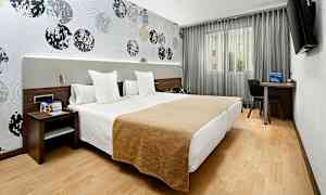 Et hotelværelse med to enkeltsenge placeret ved siden af hinanden. Væggene er dekoreret med et mønster af cirkler, og der er en tv, skrivebord og stol ved vinduet. (AI-genereret tekst)