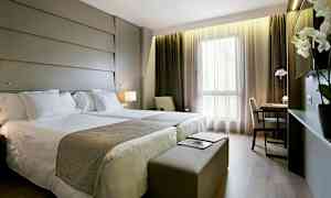 Et hotelværelse med to senge, skrivebord og store vinduer. (AI-genereret tekst)