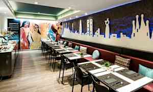 En restaurant med lang bænk og borde med duge samt dekorationer på væggene. (AI-genereret tekst)