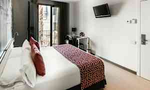 Et moderne hotelværelse med en stor seng, altandøre og et skrivebordsområde. (AI-genereret tekst)