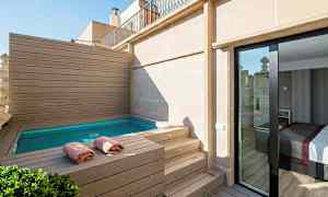 Terrasse med lille pool omgivet af træpaneler, håndklæder på kanten og glasdør, der fører ind til et værelse. (AI-genereret tekst)