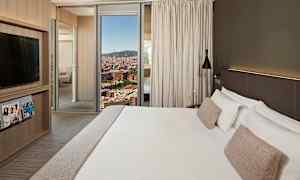 Et hotelværelse med en stor seng med hvidt sengetøj og beige puder, moderne design med et TV-skab, magasiner og et vindue, der viser en byudsigt. (AI-genereret tekst)