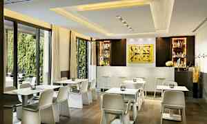 En moderne café med hvide borde og stole foran en bar i en lys indretning. (AI-genereret tekst)