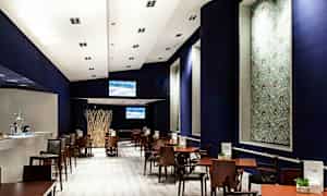 En moderne restaurant eller café med træmøbler og mørk indretning. Den viser borde og stole arrangeret i rækker under et skarpt oplyst loft. (AI-genereret tekst)