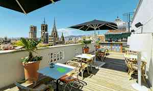 Tagterrasse med siddepladser og paraplyer, med udsigt over byens gamle bygninger og et barområde i baggrunden. (AI-genereret tekst)