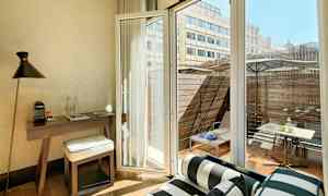 Interiør af et rum med skrivebord, stol og åben glasdør med udsigt til en terrasse med møbler. (AI-genereret tekst)