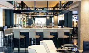 En bar i et moderne miljø med høje stole og flasker placeret på hylder. (AI-genereret tekst)