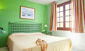 Et soveværelse med en grøn væg, en seng med beige sengetæppe, en sort sengegavl og et vindue med stribede gardiner. (AI-genereret tekst)