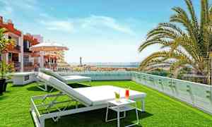 Tagterrasse med græsplæne, liggestole, et lille bord med drikkevarer og udsigt over omgivelserne. (AI-genereret tekst)