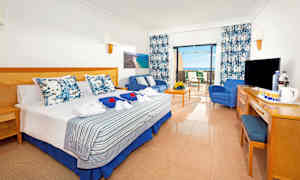 Et hotelværelse med en dobbeltseng, siddeområde og terrasse. Udsigten viser havet. (AI-genereret tekst)