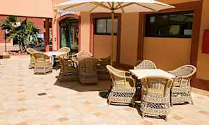 Udendørs servering med kurvemøbler og en parasol, placeret på en flisebelagt gård. (AI-genereret tekst)