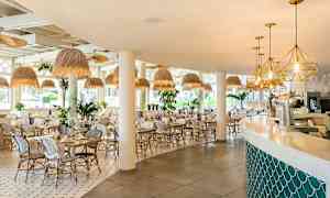 Billede af en lys og moderne restaurant med hvide stole og borde, loftslamper i naturlig stil og en bar med bløde linjer. (AI-genereret tekst)