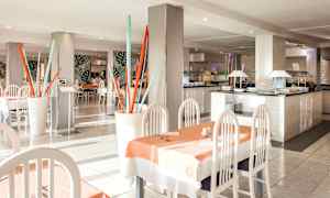 En restaurant med lyse møbler, borde dækket med duge, og dekorative elementer som farvestrålende stavinstallationer. (AI-genereret tekst)