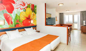 Hotelværelse med seng, farverigt vægmaleri af blomster og siddeområde med køkken. (AI-genereret tekst)