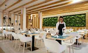 En restaurant med moderne indretning med hvide stole, dækkede borde og en væg dekoreret med planter. (AI-genereret tekst)