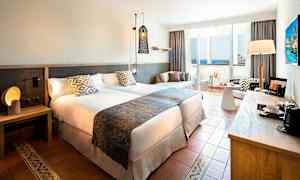 Hotelværelse med to senge, natbord, siddeområde og altan med havudsigt. (AI-genereret tekst)