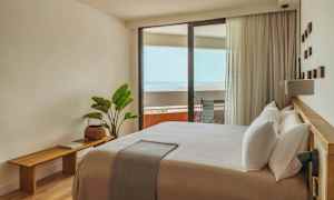 Et lyst og moderne indrettet hotelværelse med en stor seng og en balkon med udsigt over havet. (AI-genereret tekst)