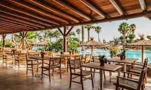 En udendørs restaurant med træmøbler og en tagterrasse, omgivet af palmer og en pool. (AI-genereret tekst)