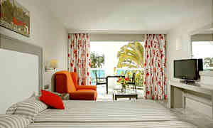 Hotelværelse med to senge, rød stol, bord og altan med udsigt. (AI-genereret tekst)