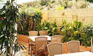 Udendørsmøbler med bord og stole af rattan foran en frodig have. (AI-genereret tekst)