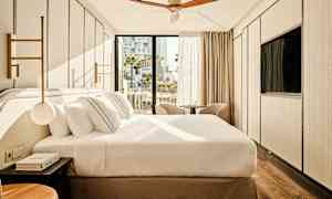 Et moderne hotelværelse med en stor seng, to stole foran vinduet og en loftsventilator. (AI-genereret tekst)