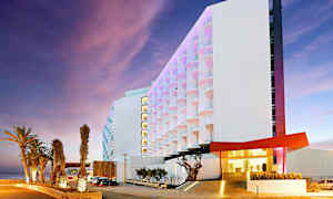 Moderne hotel med oplyste palmer ved hovedindgangen og en farverig facade. (AI-genereret tekst)