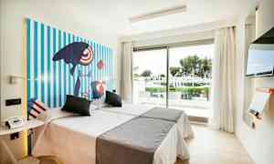 Et lyst hotelværelse med to senge, farverig kunst på væggen, en glasdør med udsigt over en frodig have og et moderne tv. (AI-genereret tekst)