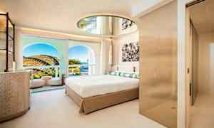 Et moderne hotelværelse med en stor seng, et rundt spejl i loftet og en balkon med udsigt over landskabet og himlen. (AI-genereret tekst)