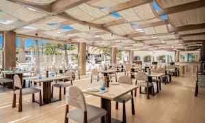 En restaurant med borde og træstole, godt oplyst med naturligt lys. (AI-genereret tekst)