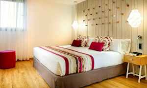 Et soveværelse med en stor seng, pyntepuder og et farvematchende sengetæppe. På væggen bag sengen er der dekorative detaljer, og til højre står et natbord. (AI-genereret tekst)