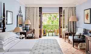 Hotelværelse med seng, skrivebord og siddeområde samt en balkon med udsigt over grønne områder. (AI-genereret tekst)