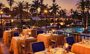 Udendørs servering med dækkede borde, omgivet af palmer ved en pool i skumringen. (AI-genereret tekst)