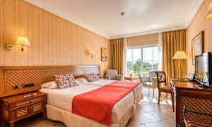 Billede af et hotelværelse med to senge, stol og bord, samt en TV. (AI-genereret tekst)