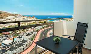 Udsigt fra en altan mod havet, med et bord og en stol. (AI-genereret tekst)