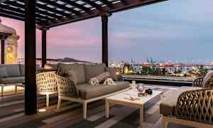 Moderne siddegruppe på terrasse med udsigt over havn og by i skumringen. (AI-genereret tekst)