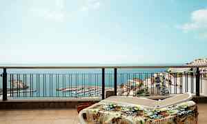 Liggestole på en terrasse med udsigt over havet og en havn. (AI-genereret tekst)