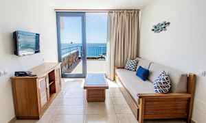 Et hotelværelse med siddeområde og udsigt til havet fra en balkon. (AI-genereret tekst)