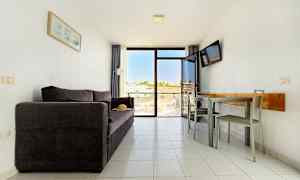 En stue med en mørk sofa, et spisebord med stole og en balkon med udsigt. (AI-genereret tekst)