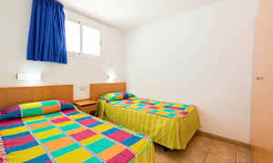 Et værelse med to enkeltsenge dækket med farverige mønstrede sengestæpper. (AI-genereret tekst)