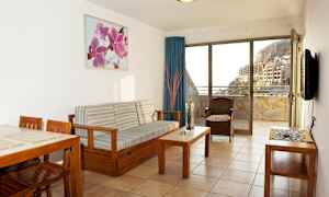 En stue med træindretning og udsigt til en altan samt bygninger og bjerge. (AI-genereret tekst)