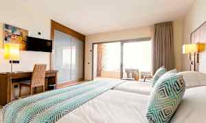 Billede af et hotelværelse med to senge, et skrivebord, et fjernsyn og en balkon med stole. (AI-genereret tekst)