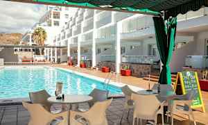 Udsigt over en swimmingpool med liggestole og borde på terrassen, omgivet af bygninger. (AI-genereret tekst)