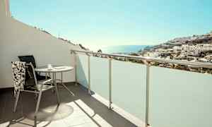 Altan med bord og stol, udsigt over hav og bygninger. (AI-genereret tekst)