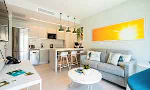 Interiør af et moderne køkken med integreret opholdsområde, grå sofa og farverigt kunstværk. (AI-genereret tekst)