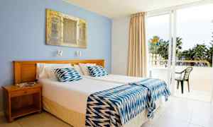 Et hotelværelse med to enkeltsenge, en blå væg og en glasdør, der fører ud til balkonen. (AI-genereret tekst)