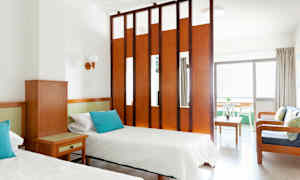 Et hotelværelse med to enkeltsenge, et træbord og en siddegruppe adskilt af en rumdeler. (AI-genereret tekst)